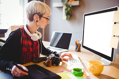 Female graphic designer using graphic tablet while working on computer at office