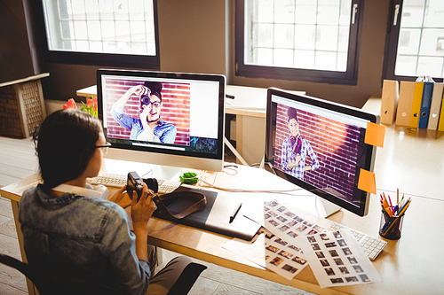 Female graphic designer holding digital camera while working at office