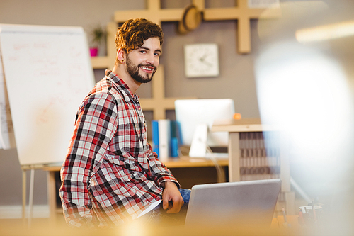 Portrait of smiling graphic designer sitting with laptop at office