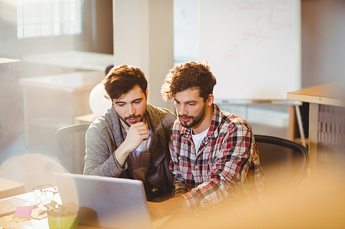 Graphic designer using laptop with his coworker in the office