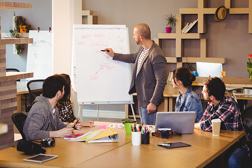 Male graphic designer discussing chart on white board with coworkers in the office