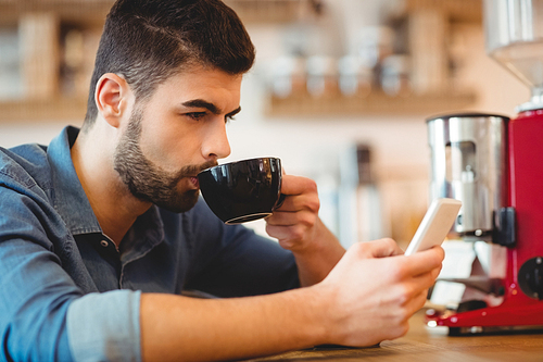 Young man text messaging on mobile phone while having coffee in office cafeteria