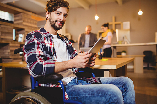 Portrait of graphic designer using digital tablet while colleagues interacting in background