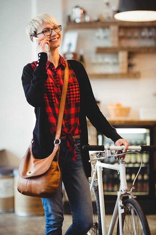 Happy young woman standing along with bicycle talking on mobile phone