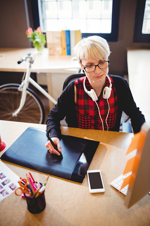 Female graphic designer using graphic tablet while working on computer at office