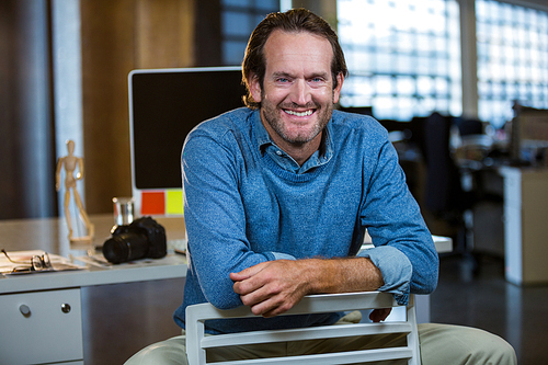 Portrait of creative businessman sitting on chair against computer desk in office