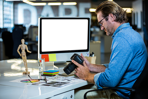 Side view of creative businessman holding camera at computer desk in office