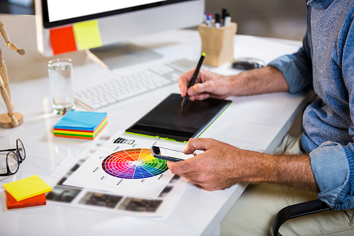 Midsection of businessman using graphics tablet at desk in creative office