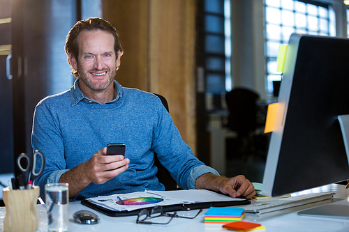 Portrait of happy businessman with cellphone at computer desk in office