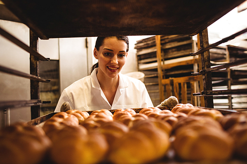 Female baker holding a tray of michetta in bakery shop