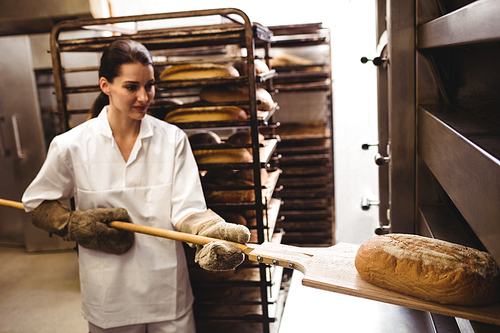 Female baker baking fresh bread in bakery shop
