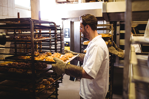 Male baker holding a tray of michetta in bakery shop