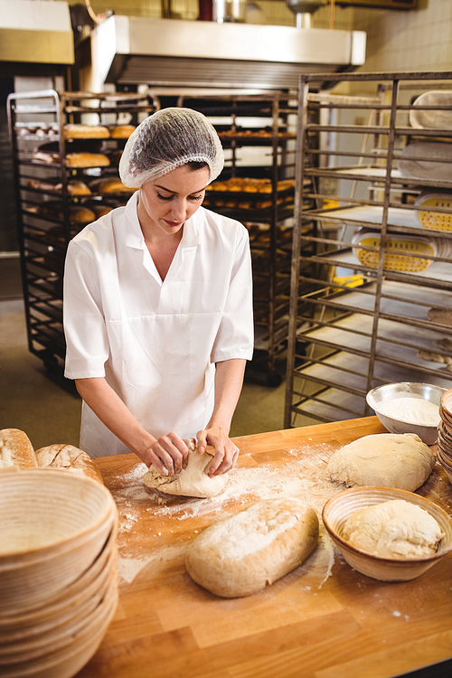 Female baker kneading a dough in bakery shop