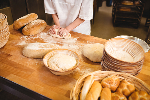 Mid-section of female baker kneading a dough in bakery shop