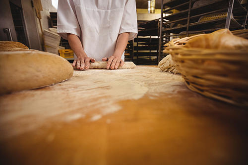 Mid-section of female baker kneading a dough in bakery shop