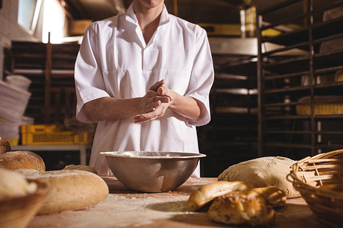Mid-section of female baker spreading flour in a bowl in bakery shop
