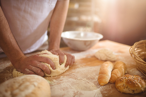 Mid-section of baker kneading a dough in bakery shop