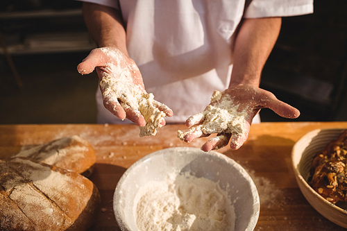 Mid-section of baker mixing flour by hand at bakery shop