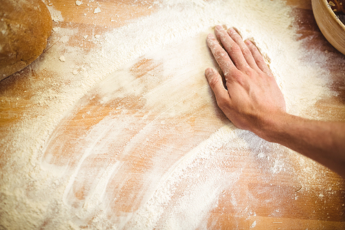 Hand of baker rubbing flour on the table at bakery shop