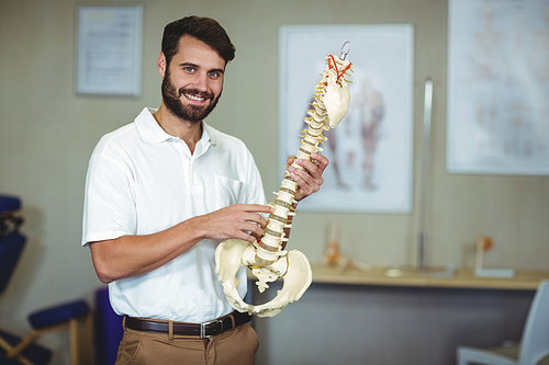 Portrait of male therapist holding spine model in clinic