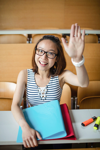 Portrait of young woman raising hand in classroom at college