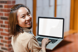 Portrait of happy young woman using laptop in corridor at college