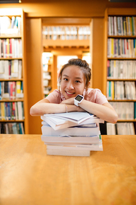 Portrait of happy young woman leaning on stack of book in library at college