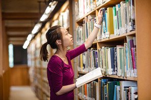 Young woman selecting book in library at college
