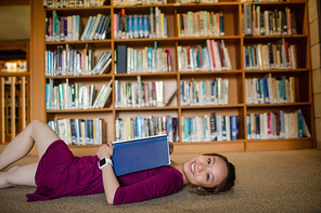 Portrait of happy young woman lying on floor in library at college
