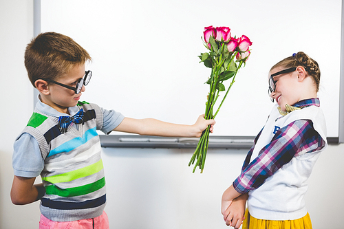 Schoolboy giving a bunch of flowers to a girl in classroom at school