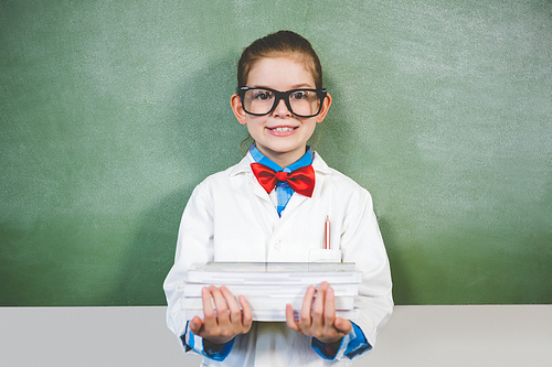 Portrait of smiling girl standing with a stack of books in classroom at school