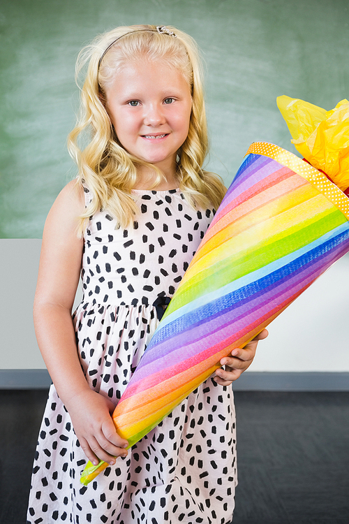 Portrait of smiling schoolgirl holding gift in classroom at school