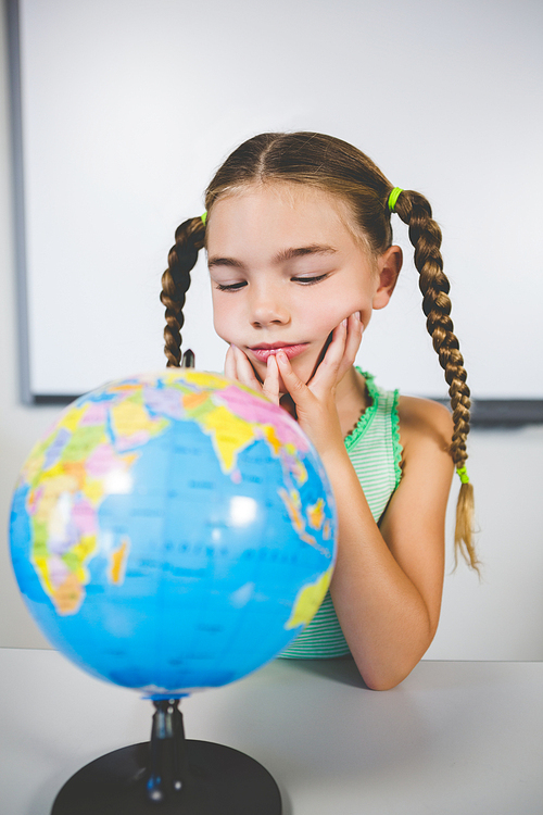 Schoolgirl looking at globe in classroom at school
