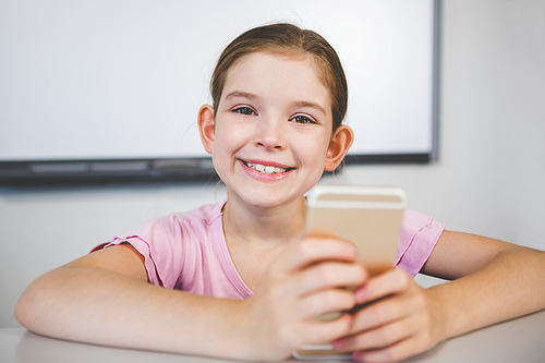 Portrait of smiling schoolgirl using mobile phone in classroom at school