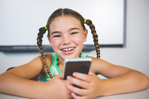 Portrait of smiling schoolgirl using mobile phone in classroom at school