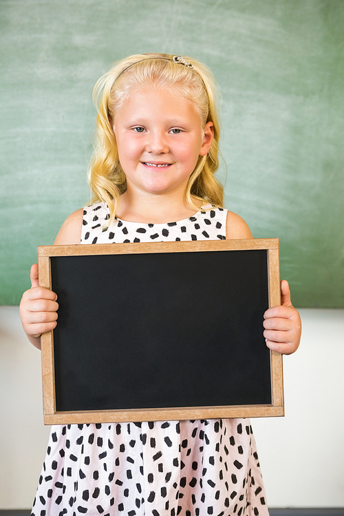 Portrait of smiling schoolgirl holding slate in classroom at school