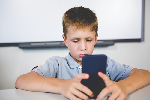 Schoolboy using mobile phone in classroom at school