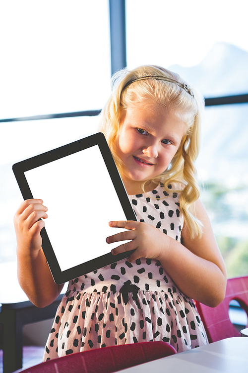 Portrait of schoolgirl showing digital tablet in classroom at school