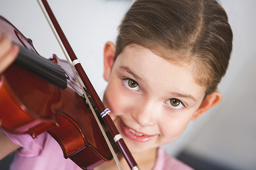 Portrait of smiling schoolgirl playing violin in classroom at school