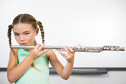 Portrait of smiling schoolgirl playing flute in classroom at school
