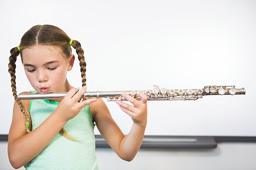 Schoolgirl playing flute in classroom at school