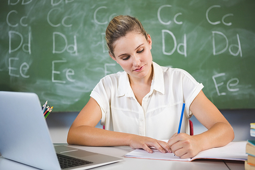 School teacher checking book in classroom at school