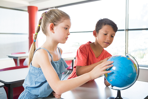 School kids looking at globe in classroom at school