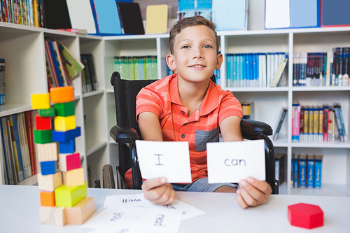 Disabled boy showing placard that reads I Can in library at school