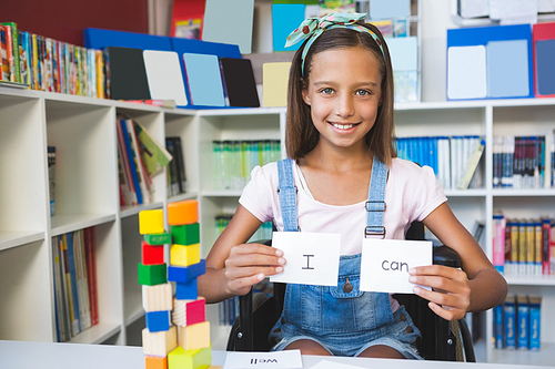 Disabled girl showing placard that reads I Can in library at school