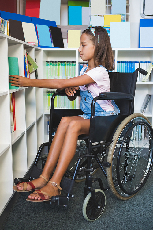 Disabled school girl selecting a book from bookshelf in library at school