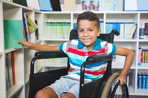 Portrait of disabled boy selecting a book from bookshelf in library at school