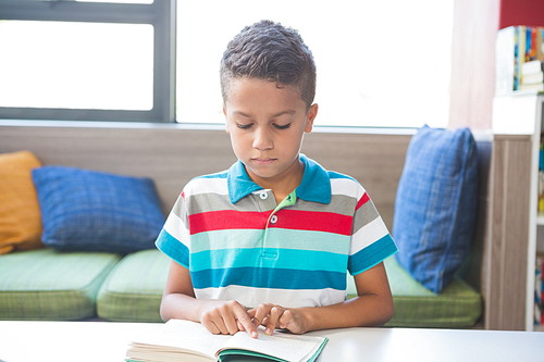 Schoolboy reading a book in library at school