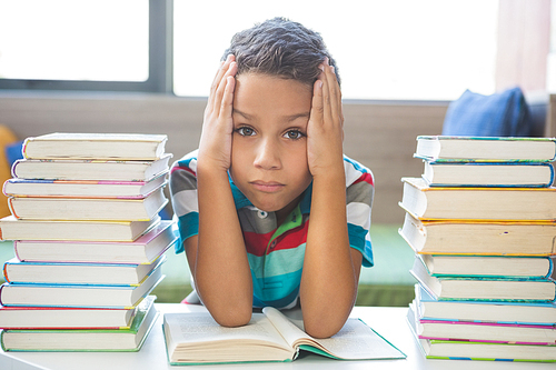 Portrait of schoolboy reading a book in library at school