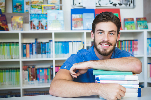 Portrait of school teacher sitting with books in library at school